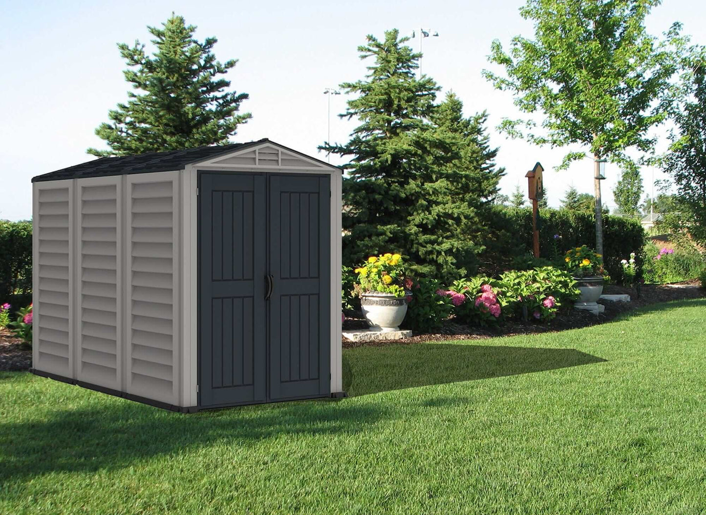 Duramax Vinyl Shed 5x8 YardMate Plus in garden setting surrounded by trees and flowers.