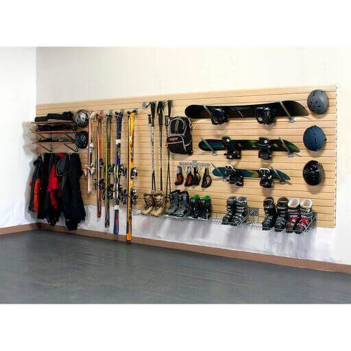 Wall storage system featuring gear like skis, snowboards, helmets, and jackets organized on a slatwall for optimal accessibility. 