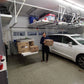 Person using Auxx Lift in garage to elevate boxes, showcasing a motorized garage storage lift for easy organization.