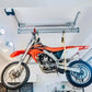 Motorized garage storage lift holding an orange dirt bike, maximizing space and safety with the Auxx-One Lift.