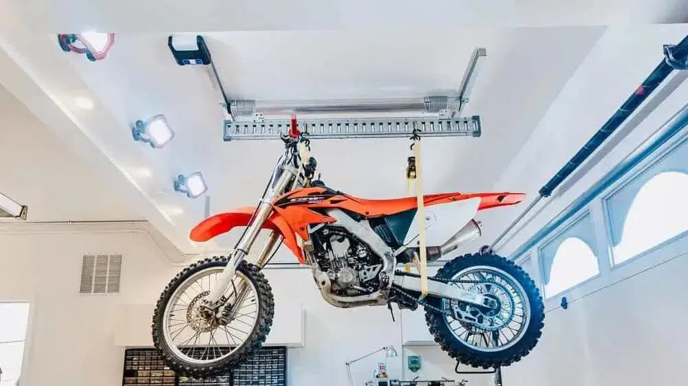 Motorized garage storage lift holding an orange dirt bike, maximizing space and safety with the Auxx-One Lift.