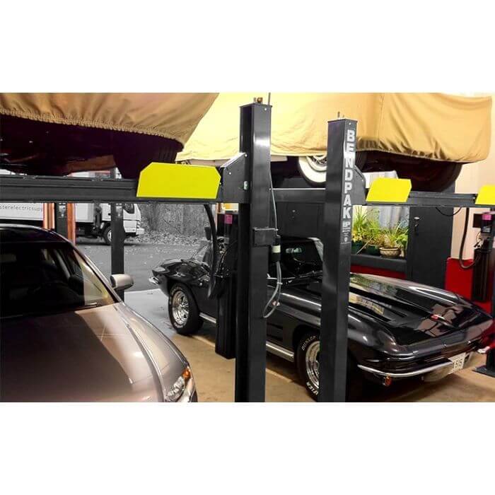 BendPak HD-7P 4 Post Car Lift showcasing two cars parked in a compact garage, emphasizing space-saving design.