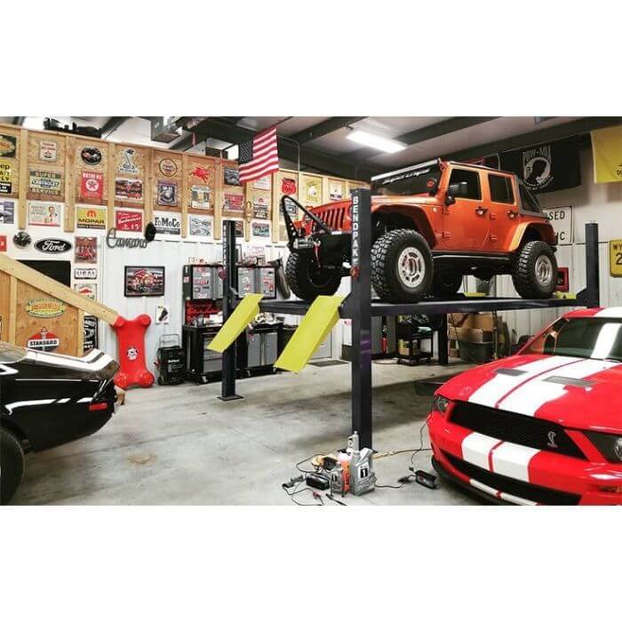 BendPak HD-9 four-post car lift in garage with Jeep Wrangler and classic cars.