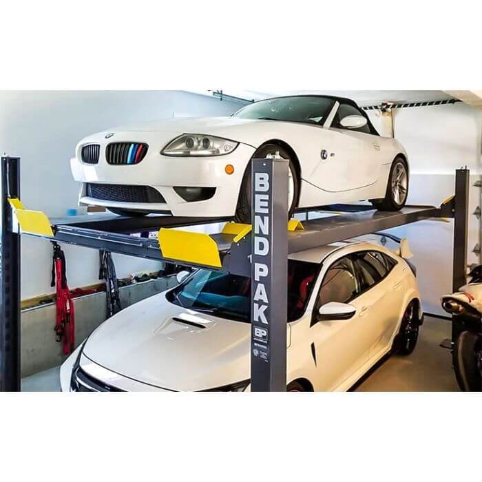 BendPak HD-9 four-post car lift showing two vehicles, one lifted, showcasing 9000-lb capacity and robust construction.