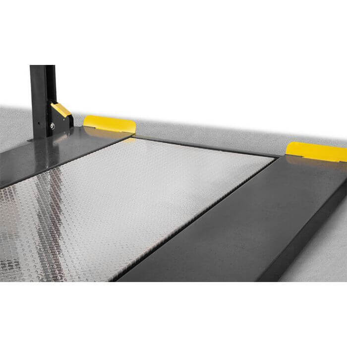 Close-up view of the BendPak HD-9XW four-post car lift platform with textured metal surface and safety yellow edges.