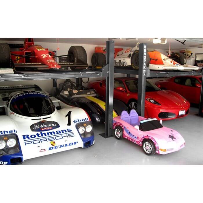 BendPak HD-9XW four-post car lift with race cars and a children's ride-on car in a garage.