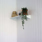 White corner shelf with a potted plant, woven baskets, and a photo frame against a lined wall.