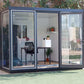 Duramax 10x10 Glass Garden Room 32001 with interior desk and chairs, surrounded by greenery.