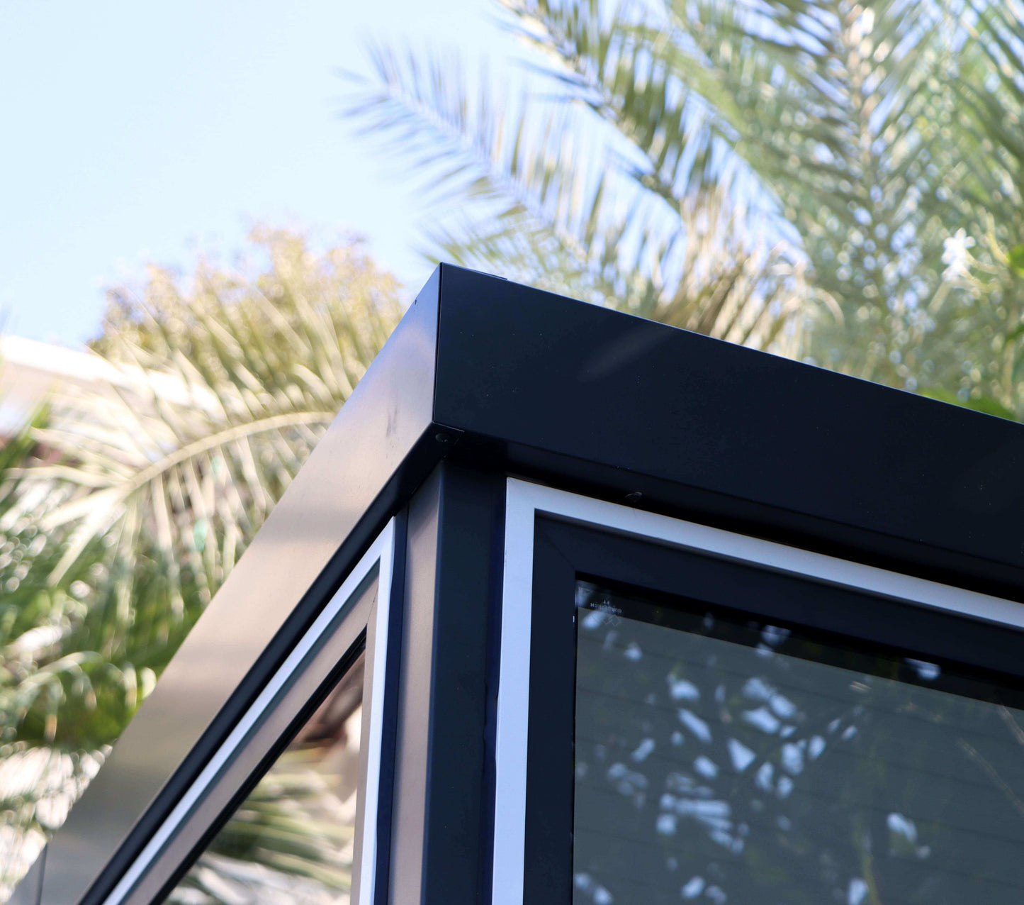 Close-up of Duramax 10x10 Glass Garden Room roof detail with palm leaves in the background.