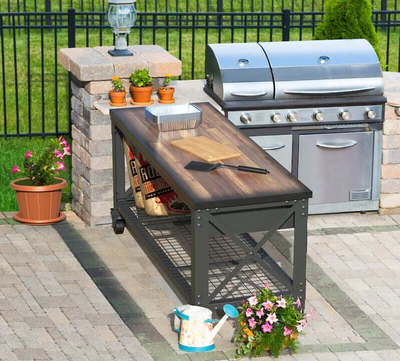 Outdoor industrial workbench with wooden top beside a grill and potted plants in a patio setting.