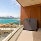 Duramax Storeaway 850L brown garden shed on a balcony with a scenic view of the city and waterfront.