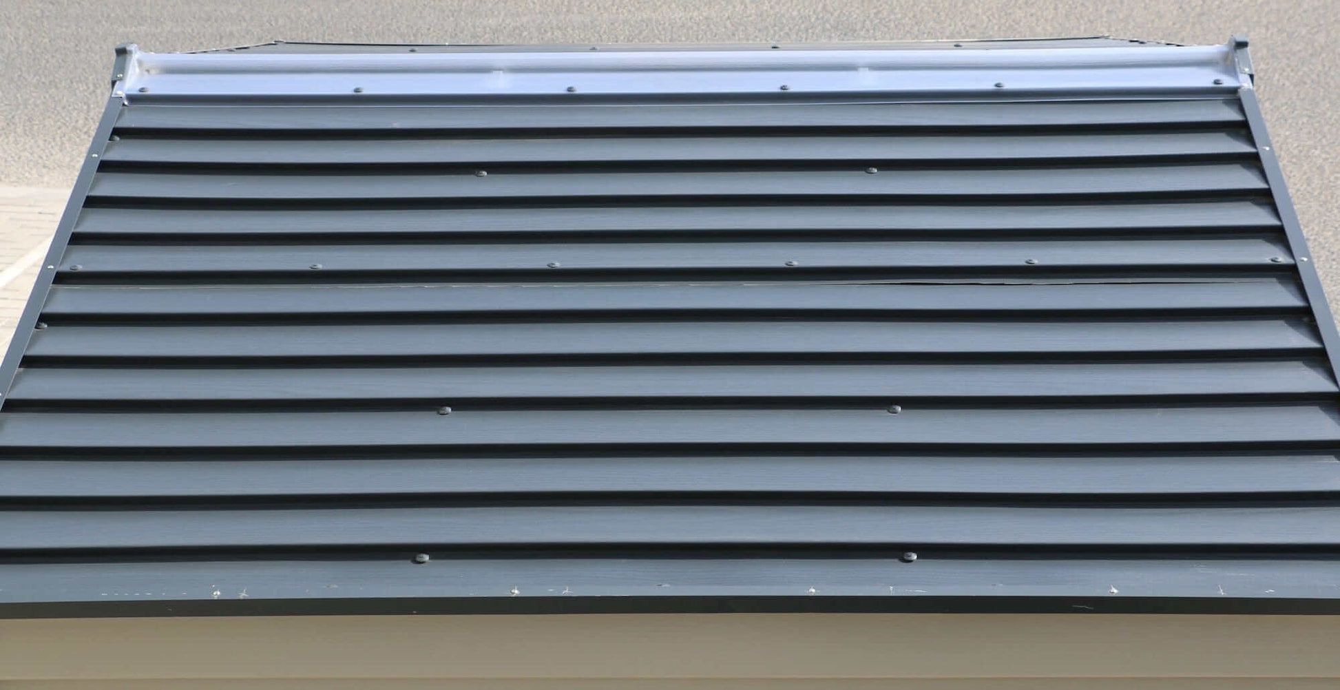 Top view of a dark gray corrugated shed roof with horizontal lines and fasteners.