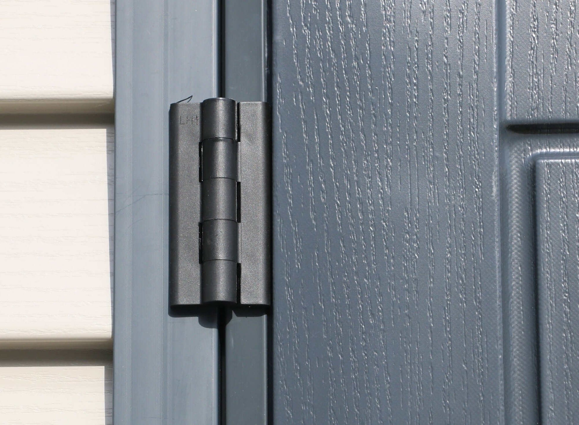 Close-up of a durable black hinge on a gray vinyl shed door.