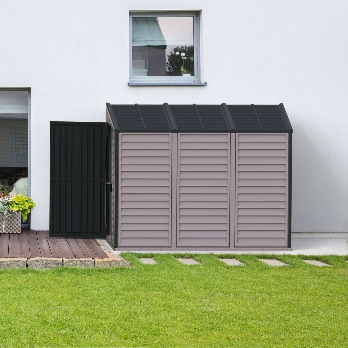 Duramax Vinyl Shed 4x8 SideMate Plus in gray with a black door, placed on a lawn next to a house.