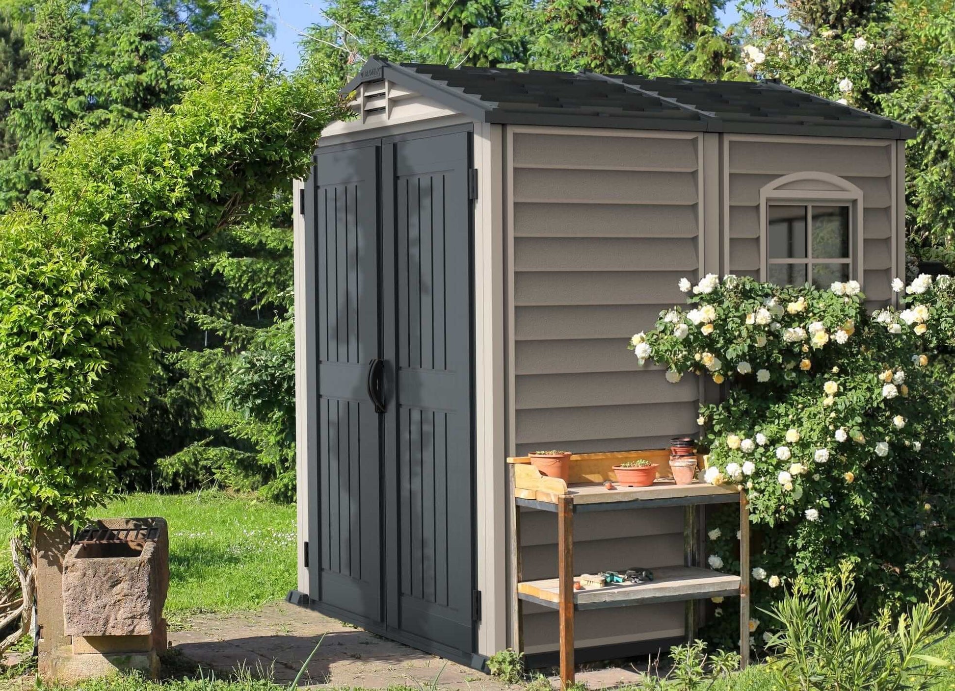 Duramax Vinyl Shed 6x6 StoreMate Plus in a garden setting surrounded by greenery and flowers.