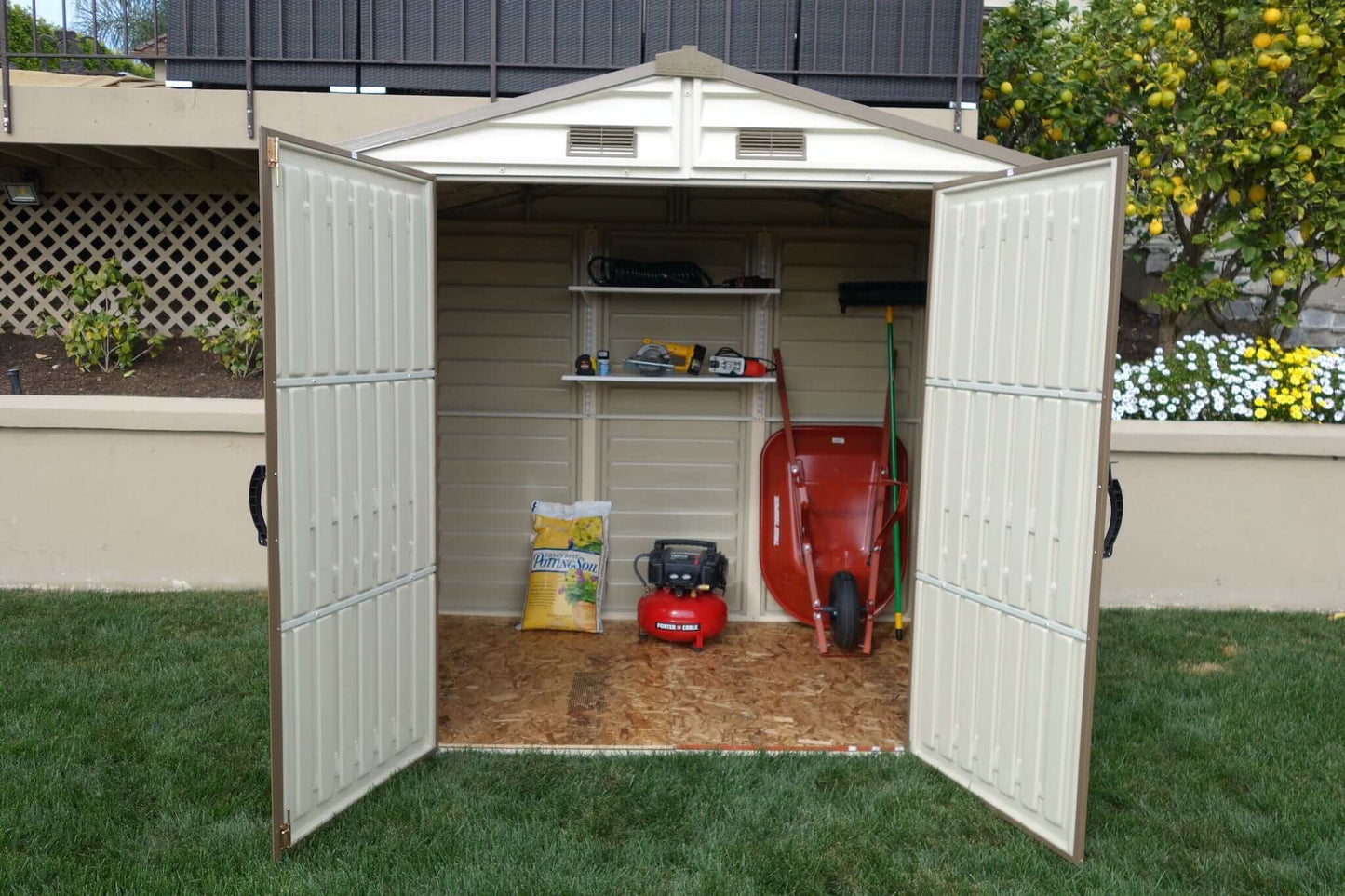 Duramax 8x6 Vinyl Shed interior with shelves, wheelbarrow, and garden tools, ideal for outdoor storage.