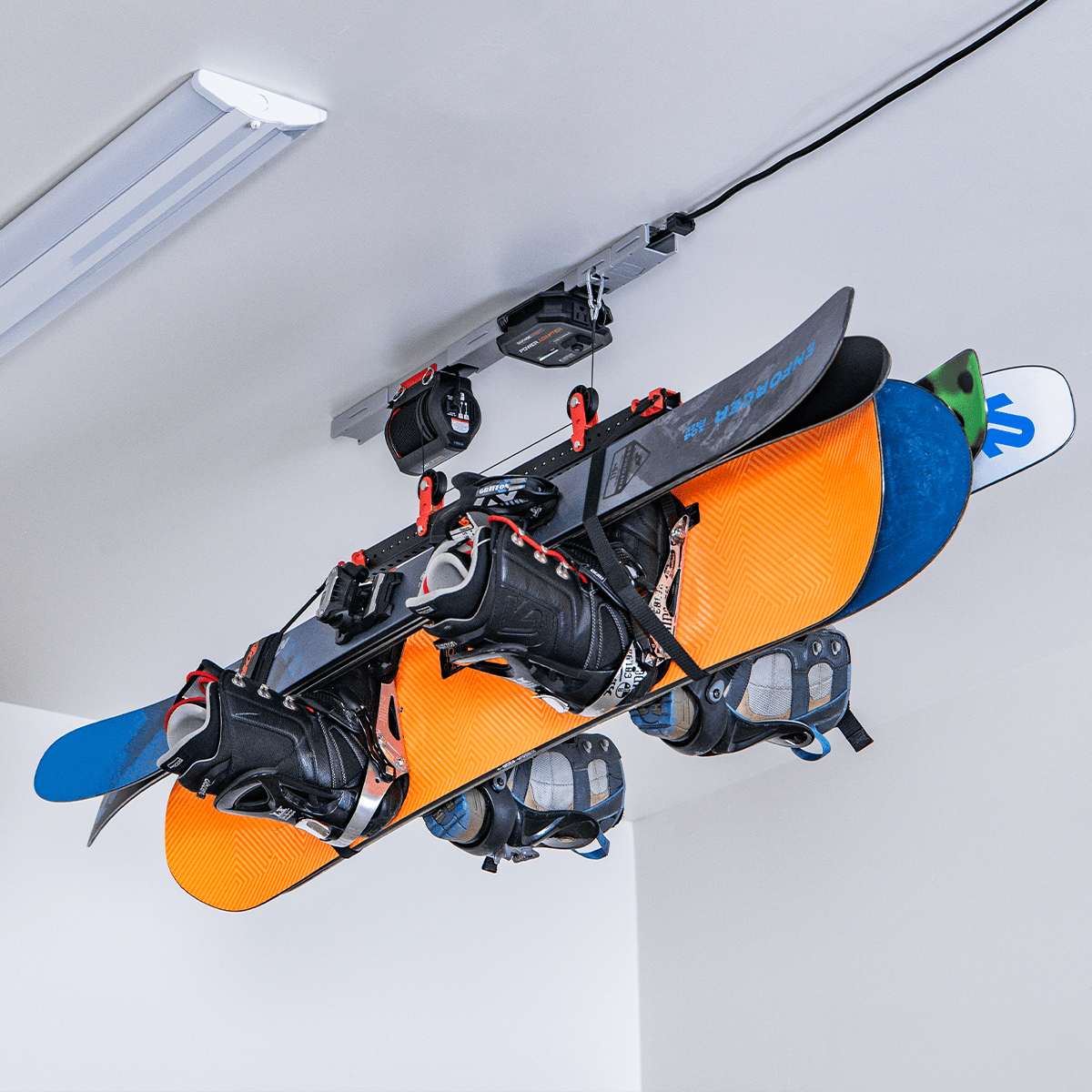 Motorized garage storage lift holding multiple snowboards with bindings, maximizing vertical space in a garage.