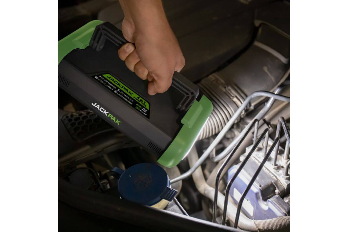 Person using JackPak ULTRA2500A jump starter under a vehicle hood to start a car.
