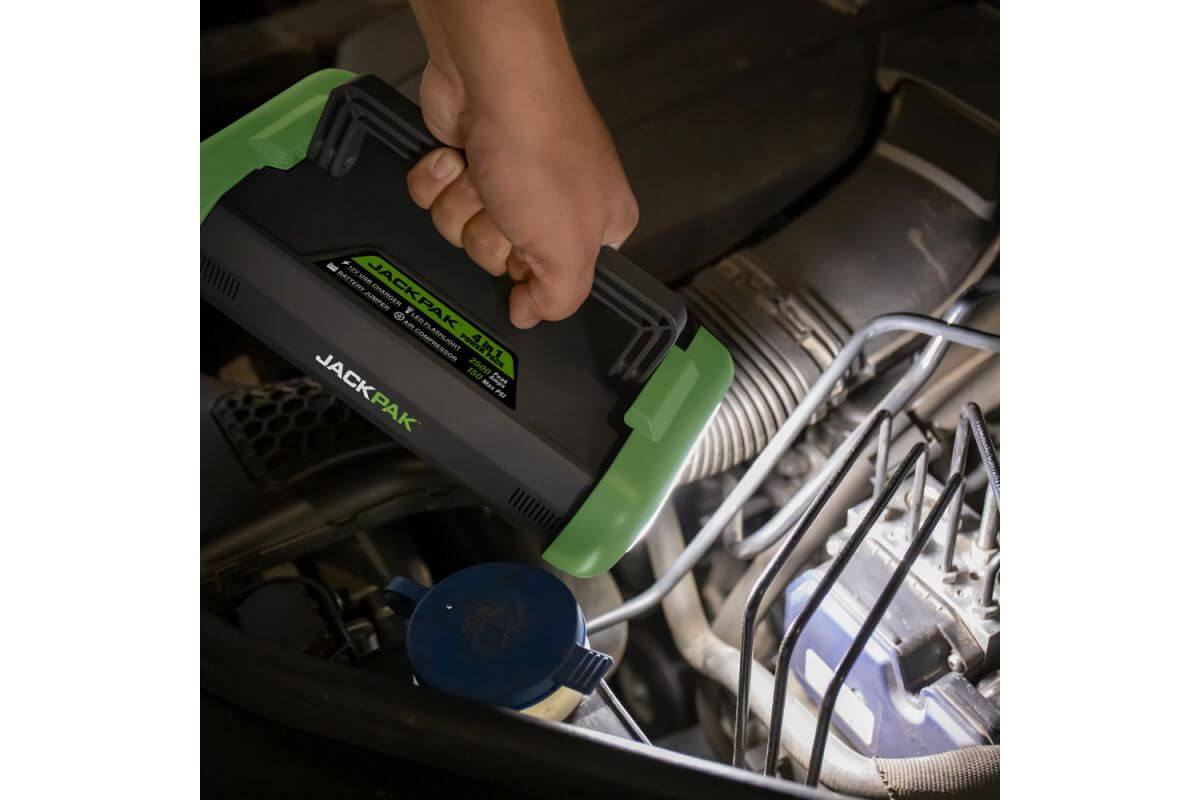 Person using JackPak ULTRA2500A jump starter under a vehicle hood to start a car.