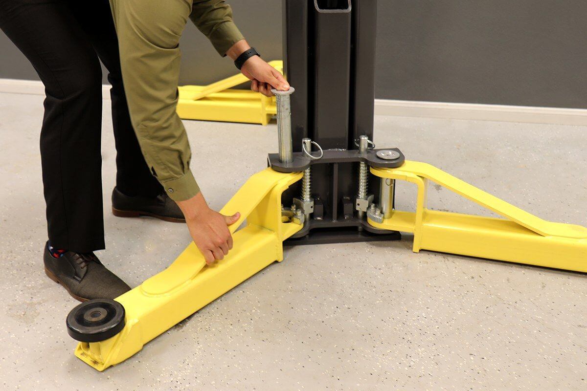 A person adjusting the safety features on the MaxJax M7K portable 2 post car lift with bright yellow arms.