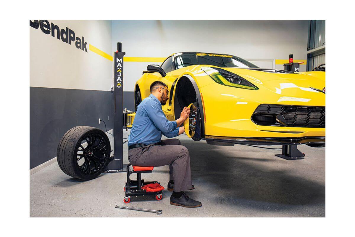 MaxJax M7K 2 Post Car Lift in action with a mechanic working on a yellow sports car's wheel.