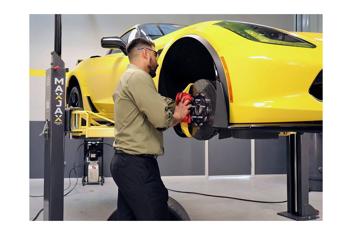 Technician using MaxJax M7K car lift for wheel maintenance on a yellow sports car.