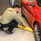 A technician using a yellow jack to lift a red car in a garage, showcasing MaxJax M7K's portability and safety features.