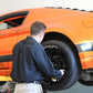 Mechanic working on an orange sports car lifted with MaxJax M7K portable car lift in a garage.