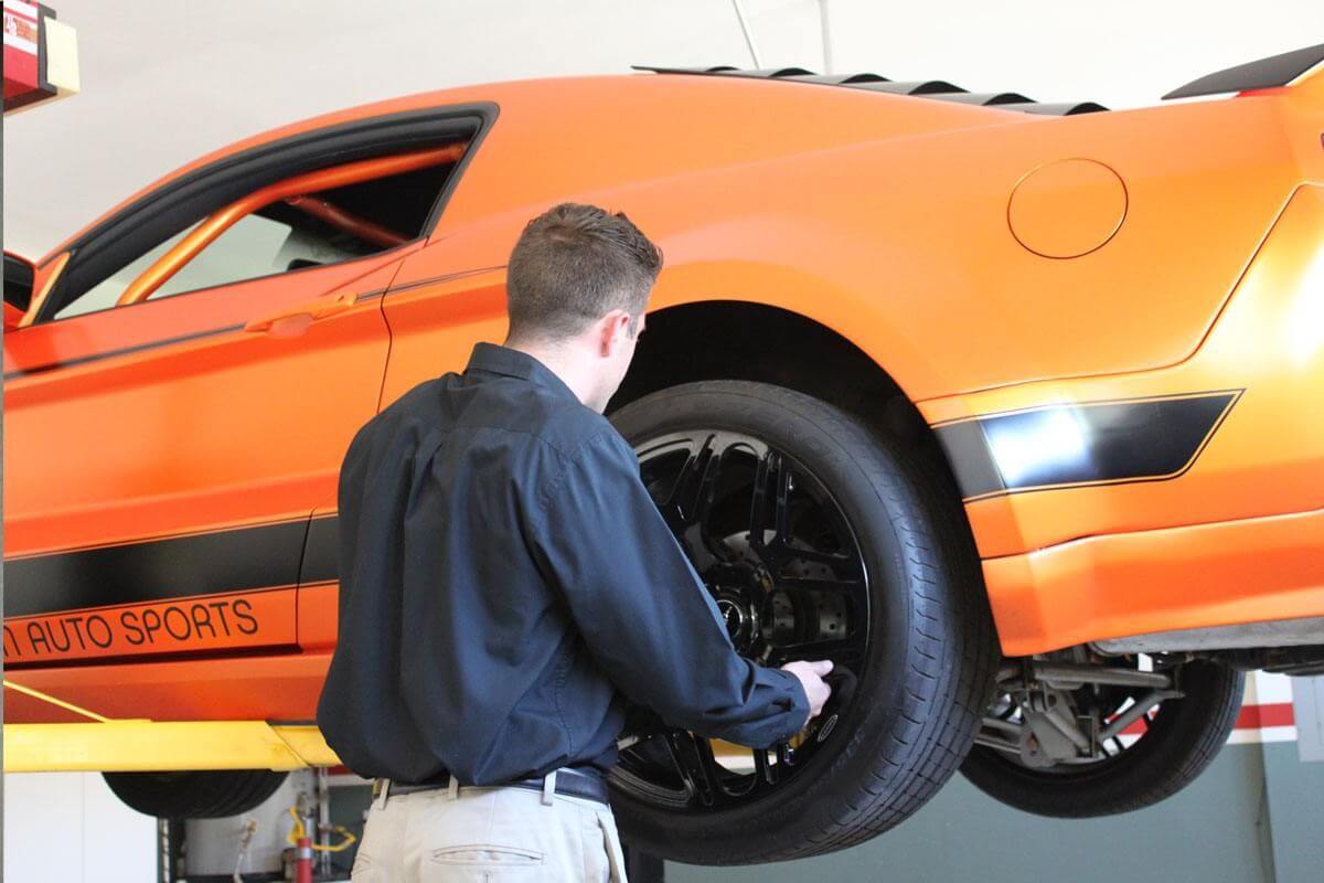 Mechanic working on an orange sports car lifted with MaxJax M7K portable car lift in a garage.