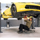 Mechanic working under a yellow car lifted by the MaxJax M7K 2 Post Car Lift in a professional garage.