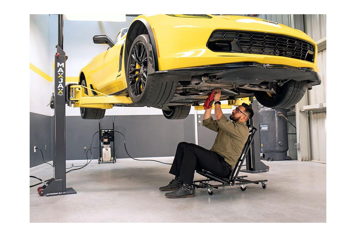 Mechanic working under a yellow car lifted by the MaxJax M7K 2 Post Car Lift in a professional garage.