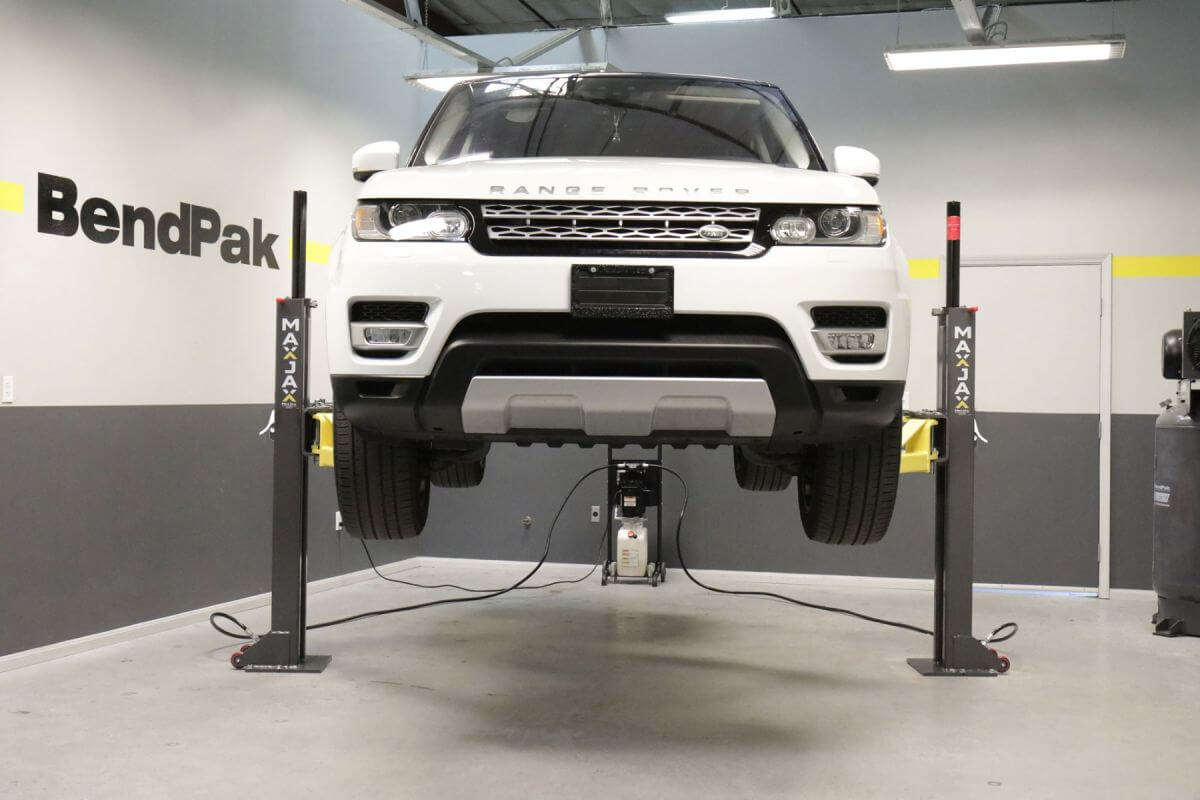 MaxJax M7K 2 post car lift in a professional garage lifting a white SUV.