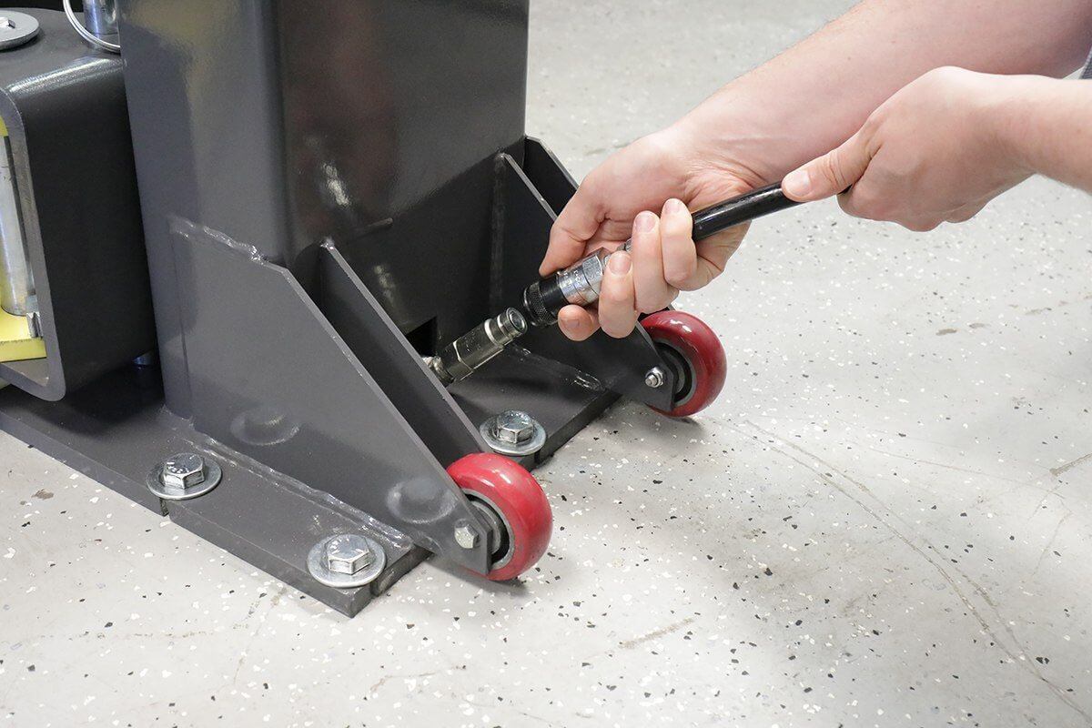 Close-up of a person using a wrench on the base of a MaxJax M7K two post car lift with red wheels.