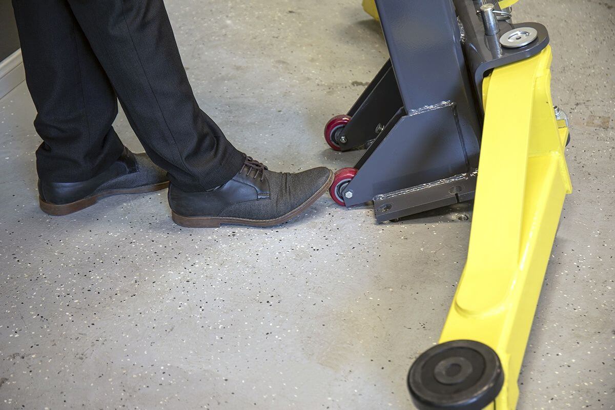 Foot activating MaxJax M7K 2 post car lift on a garage floor, showcasing safety and ease of use.