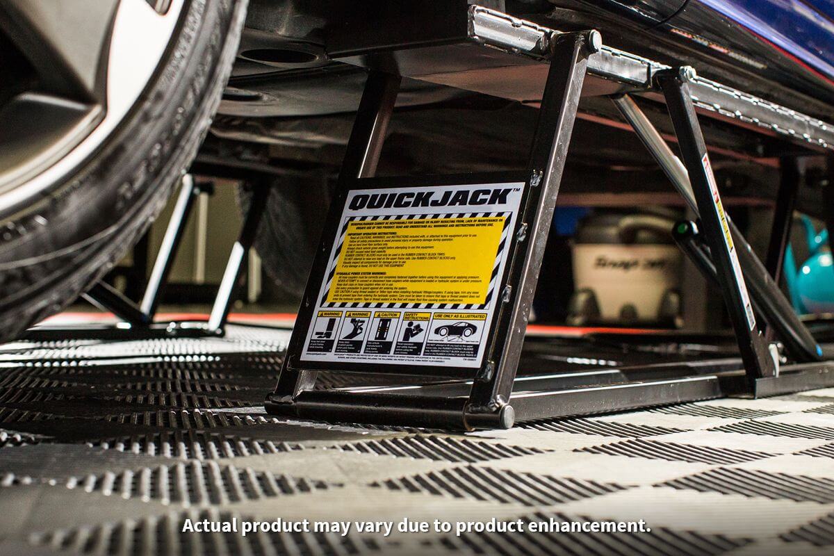 Close-up of QuickJack 7000TL portable car lift displaying safety instructions and supporting a vehicle.