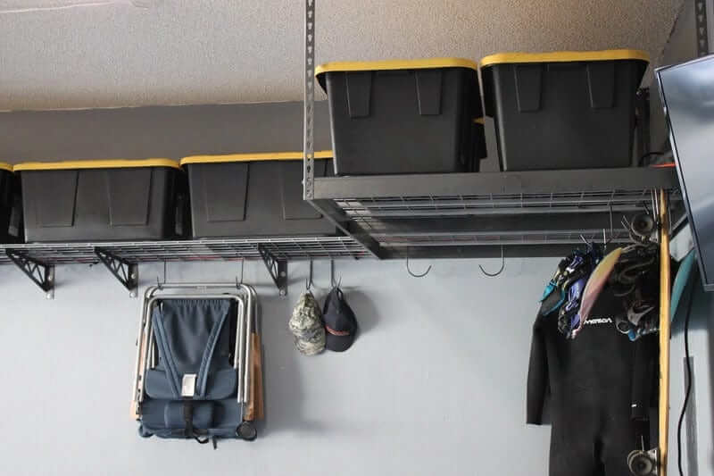 Overhead garage storage with black and yellow storage bins, folding chairs, and wetsuits hanging on hooks.