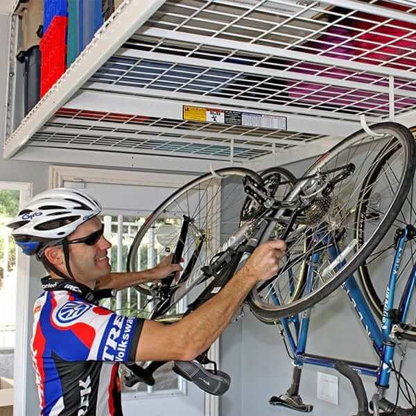 Man placing a bike on the SafeRacks 4'x8' overhead storage rack in a garage.